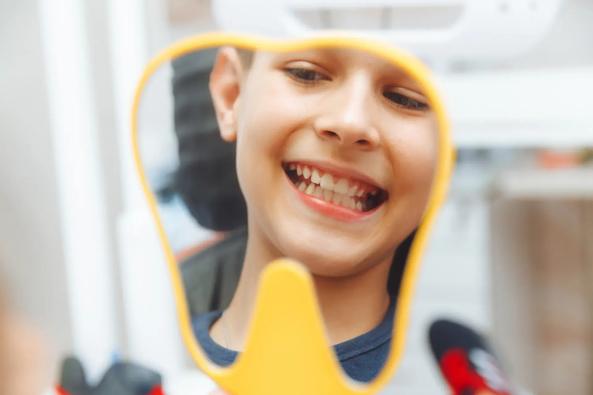 Smiling child looking at their teeth in a handheld mirror